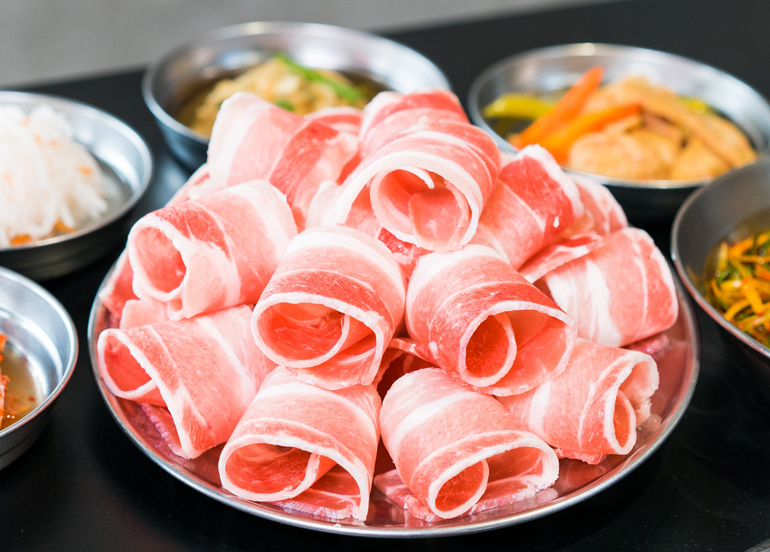 Samgyupsal on a big plate with side dishes surrounding it