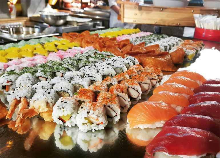 an assortment of maki, sushi, and inari topped with fresh salmon, tuna, sesame seeds, and nori flakes