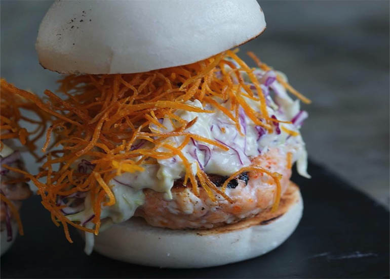 Nikkei's Salmon Burger made with steamed buns, wasabi coleslaw, sweet potato strings, and fries.